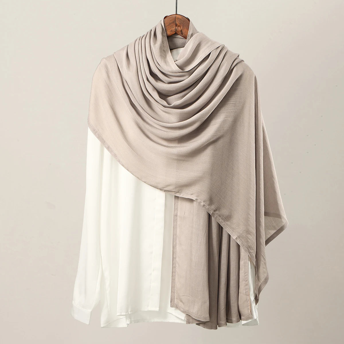 Pañuelo hijab de modal rayón beige drapeado sobre una blusa blanca, mostrado contra un fondo neutro.