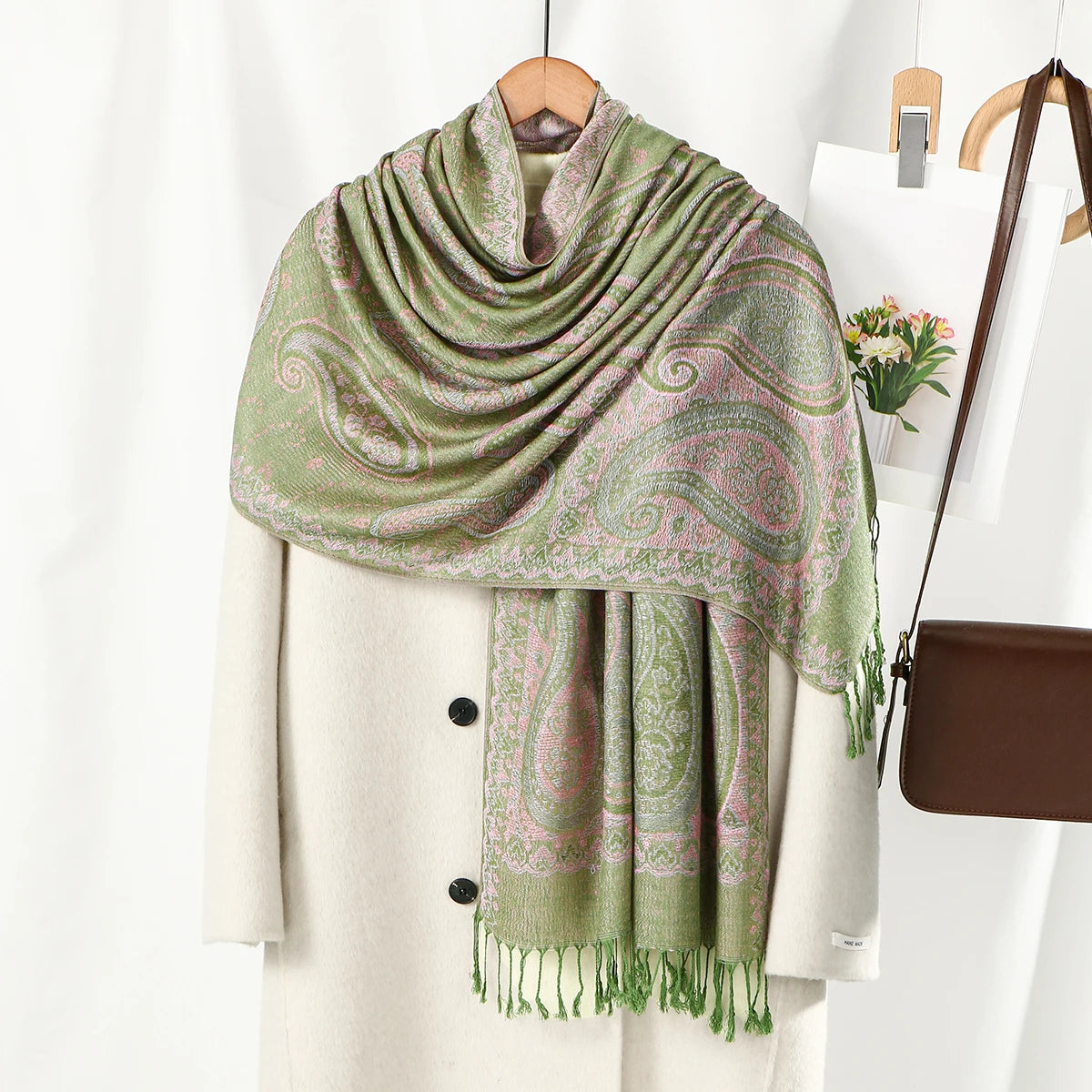 Chal de bordado paisley verde suave y rosa drapeado sobre un abrigo crema.