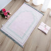 Una alfombra de oración musulmana rosa con ribete decorativo y una alfombra doblada a juego sobre un suelo de madera.