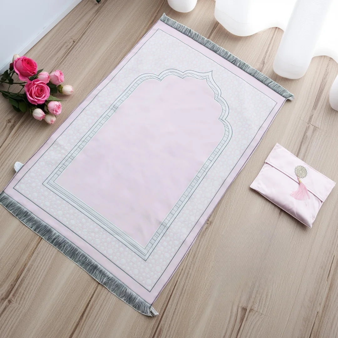 Una alfombra de oración musulmana rosa con ribete decorativo y una alfombra doblada a juego sobre un suelo de madera.