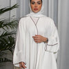Una mujer vistiendo un abaya blanca oversize con ribetes negros y un hiyab a juego, vestido modesto de largo completo.