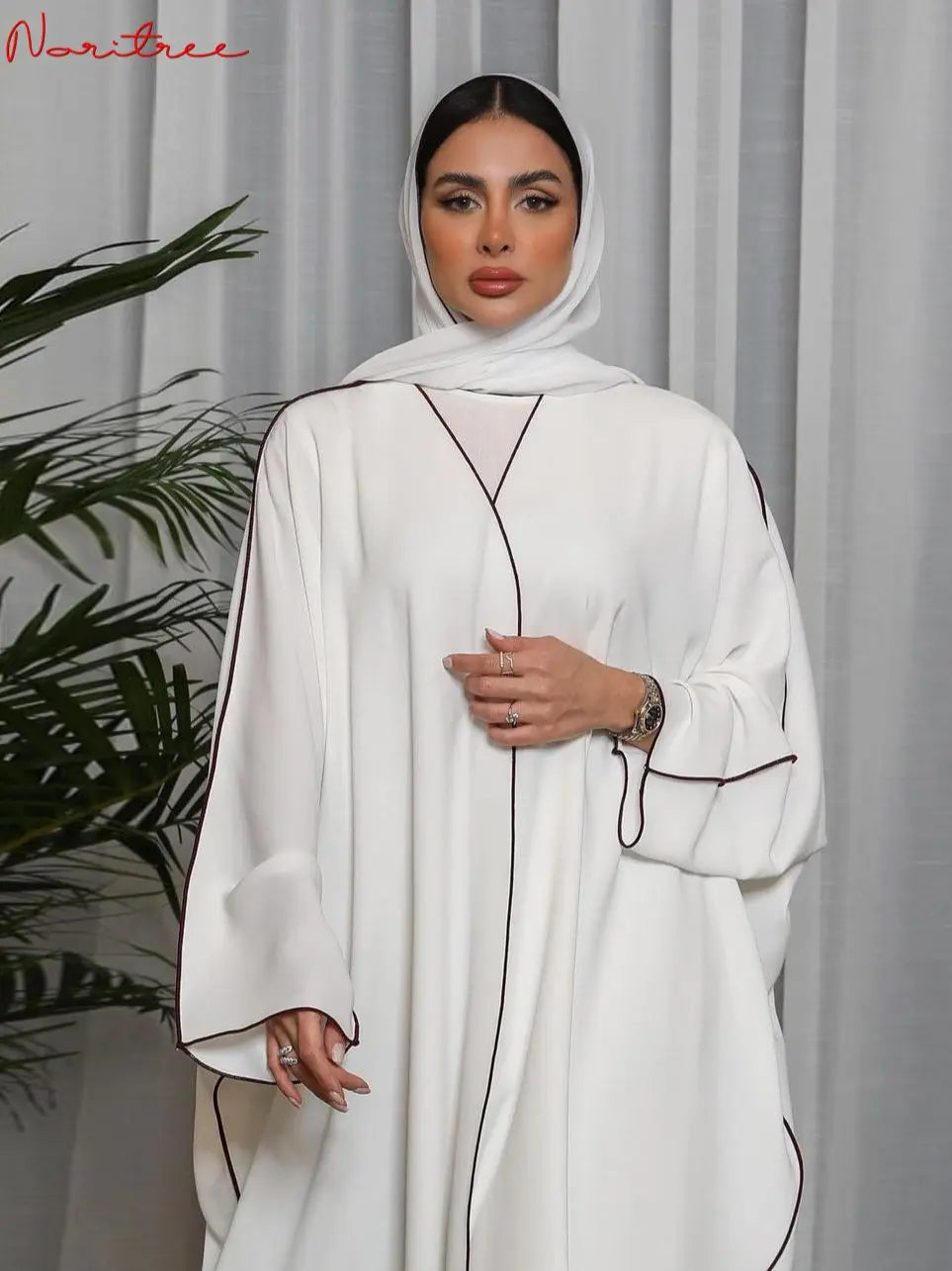 Una mujer vistiendo un abaya blanca oversize con ribetes negros y un hiyab a juego, vestido modesto de largo completo.