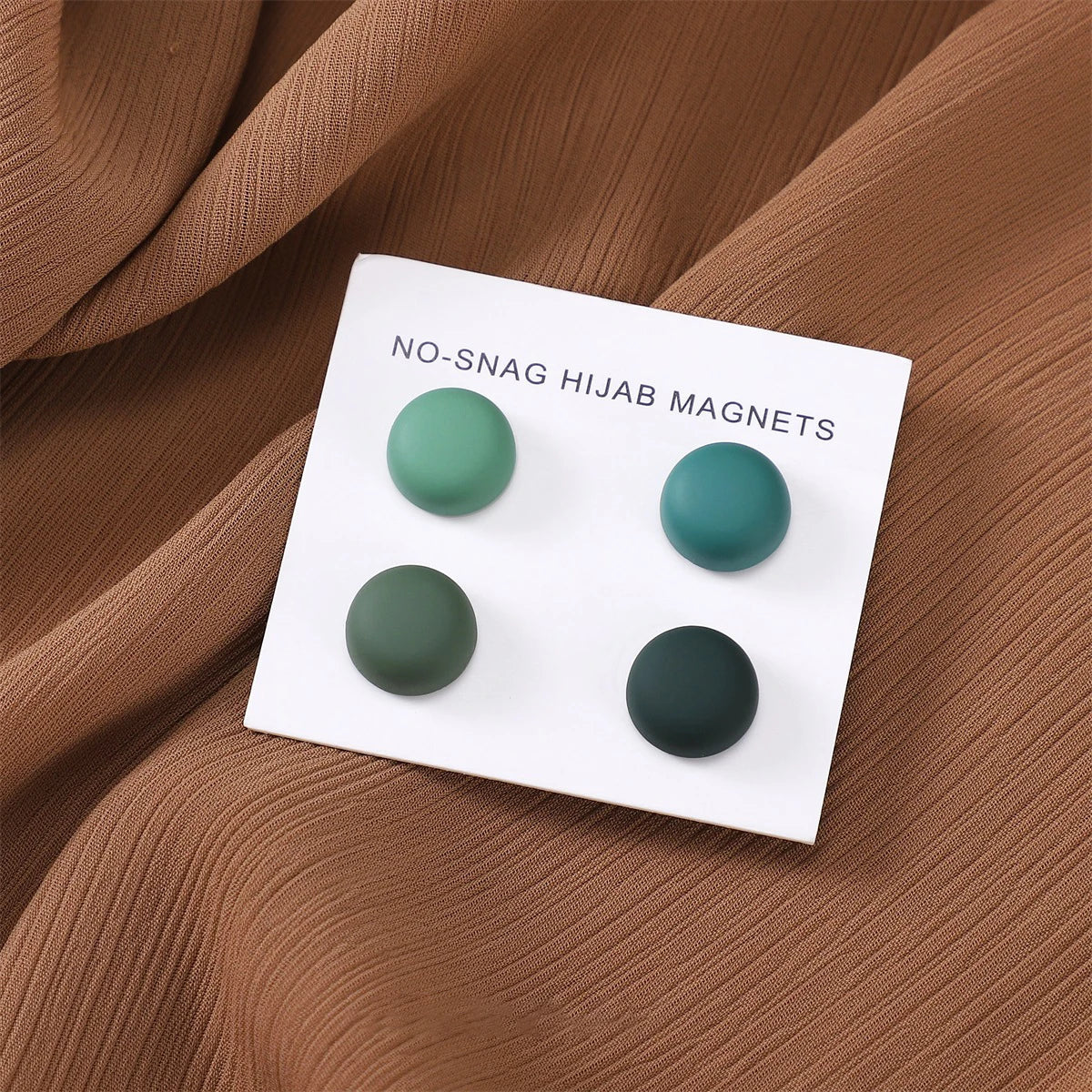 Weiße magnetische Hijab-Nadeln mit vier matten grünen Pins auf braunem Stoff.
