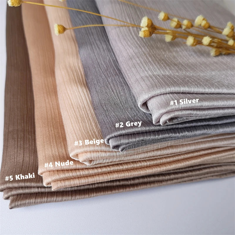 Ein Stapel aus gerüschtem Seiden-Chiffon-Hijabs in verschiedenen neutralen Tönen wie Silber, grau, beige, nude und Khaki.