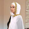 Eine Frau trägt einen weißen Spitzen-Chiffon-Hijab mit Goldstickerei über einem schwarzen Outfit.