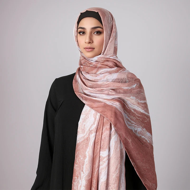 Una mujer vistiendo un pañuelo hijab con estampado acuarela rosa polvoriento y blanco, y una blusa negra.