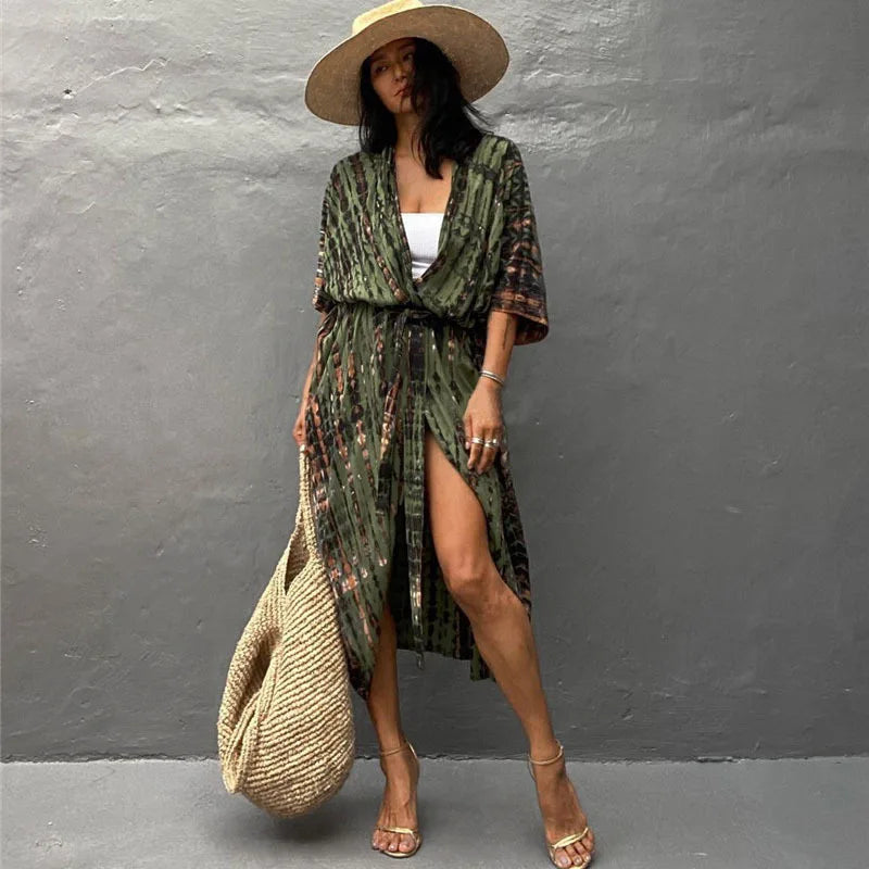 Eine Frau in einem grün-braunen gemusterten Kimono-Überkleid und Strohhut vor einer grauen Wand.