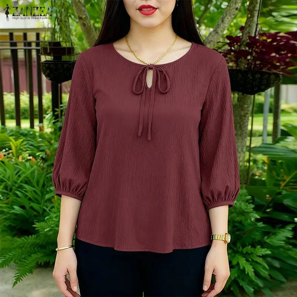 A woman models a maroon lace-up puff sleeve blouse in a casual outdoor setting.