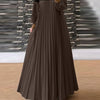 Un mannequin portant une longue caftan plissé marron avec un haut beige et des bordures noires.