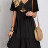 Eine Frau modelliert ein elegantes, schwarzes, A-linienförmiges Mini-Kleid mit goldener Halskette und Stroh-Schultertasche.