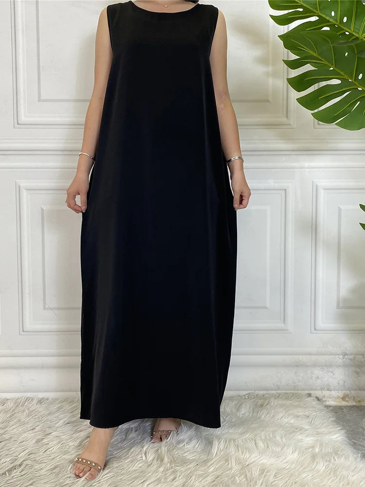 Langes, schwarzes, ärmelloses Kaftankleid gegen eine weiße vertäfelte Wand.