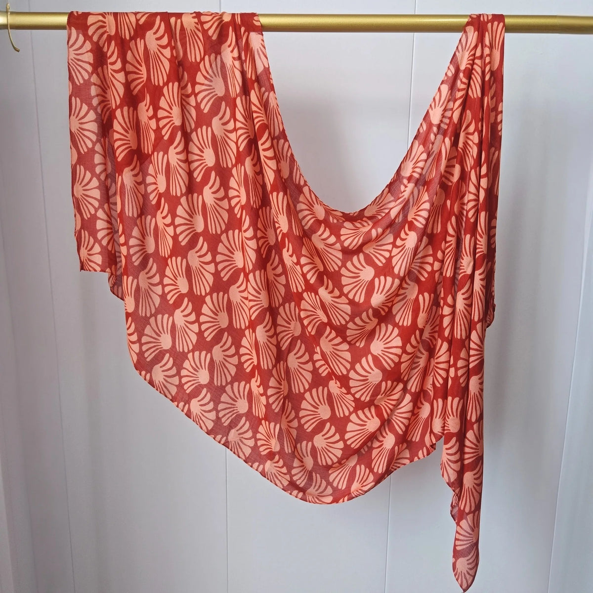 Fließender, rot-orangefarbener Hijab-Schal mit wiederkehrendem weißen Blumenmuster an einem Holzbügel hängt.