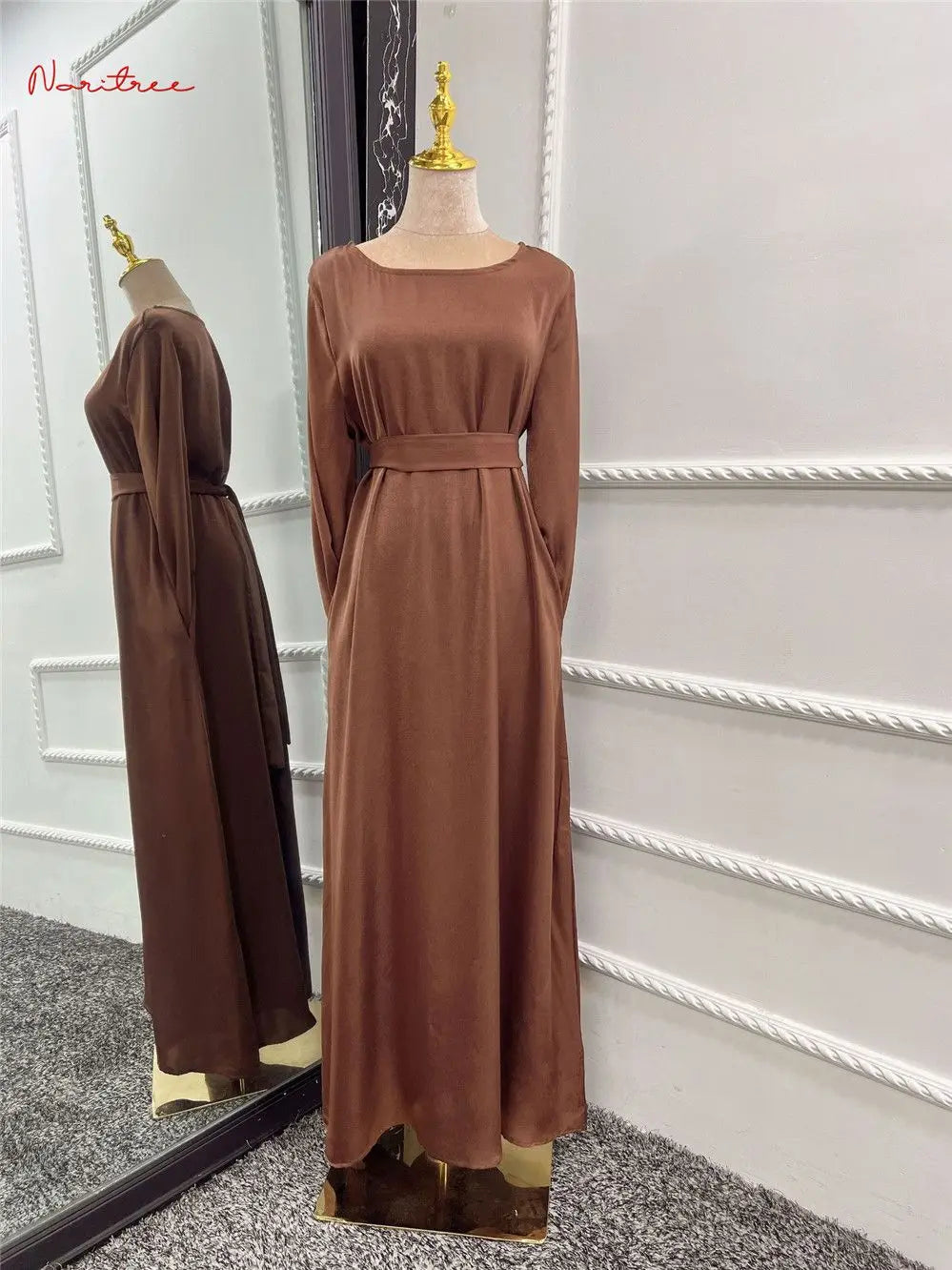Braunes, fließendes, langes Abaya-Kleid auf einem Mannequin vor weißer Wand