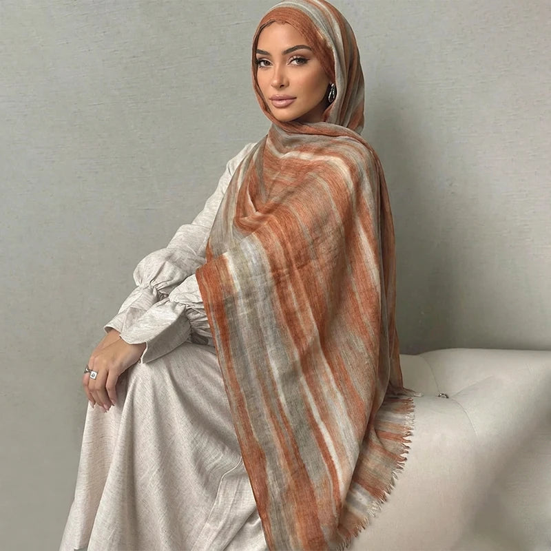 Una mujer vistiendo un pañuelo de hijab floral de acuarela bohemio a rayas naranja y beige y un conjunto a juego.