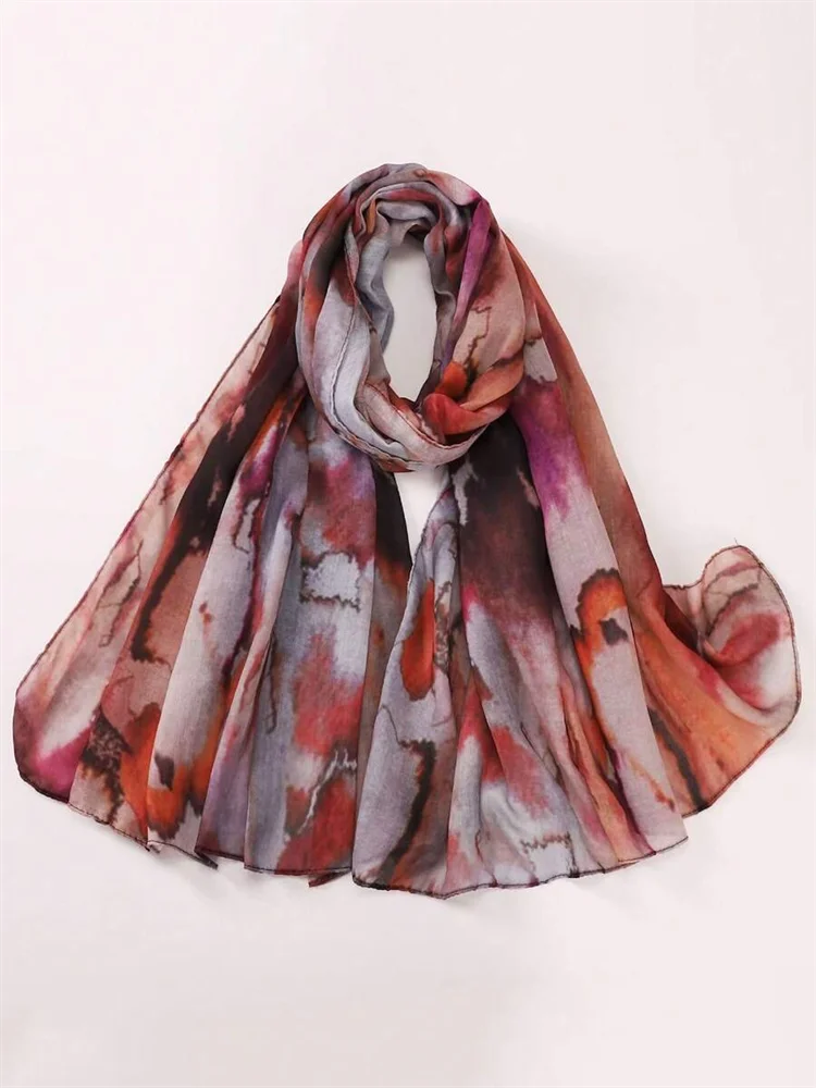 Una bufanda fluida con estampado acuarela en tonos rosa, púrpura y marrón, estilo bohemio.