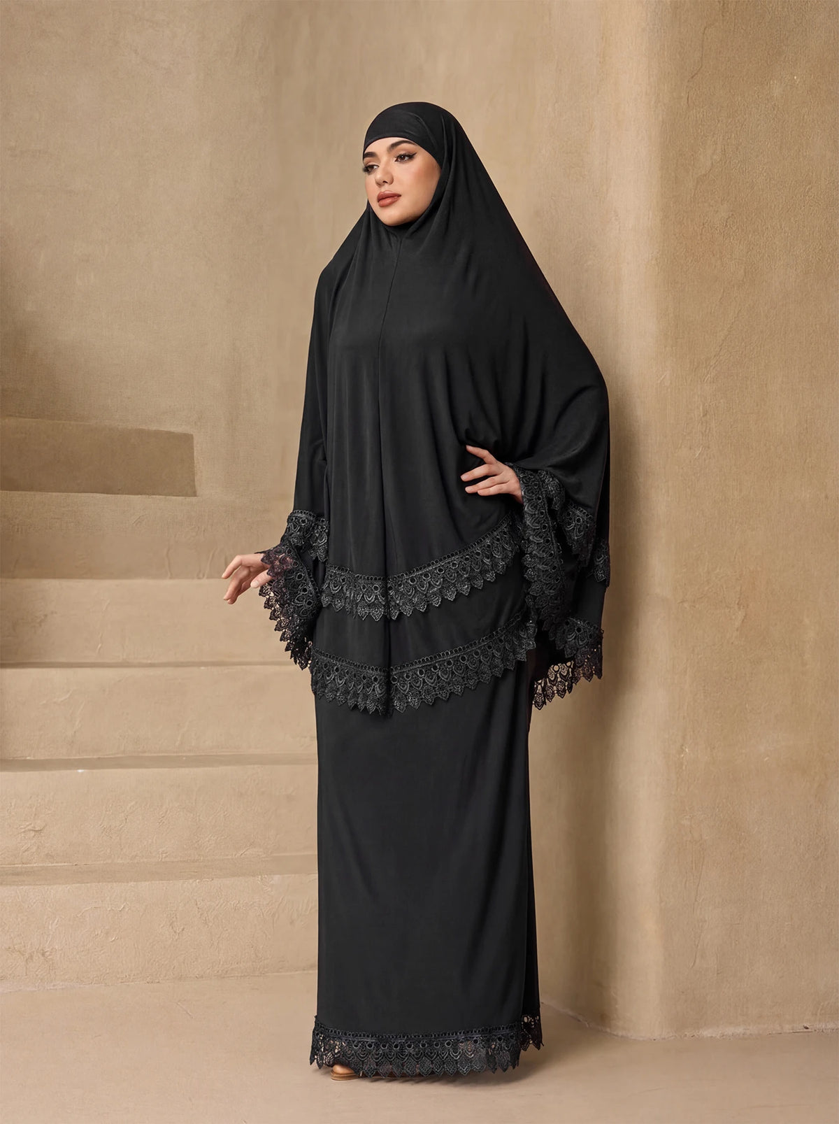 Eine Frau trägt ein elegantes schwarzes, mehrlagiges Spitzen-Khimar-Abaya-Set.