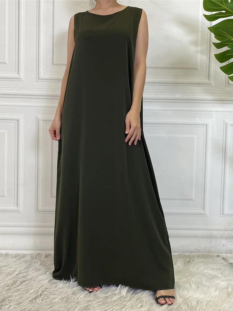 Eine Frau in einem eleganten, ärmellosen olivgrünen Kaftankleid vor einer weißen Paneelwand.