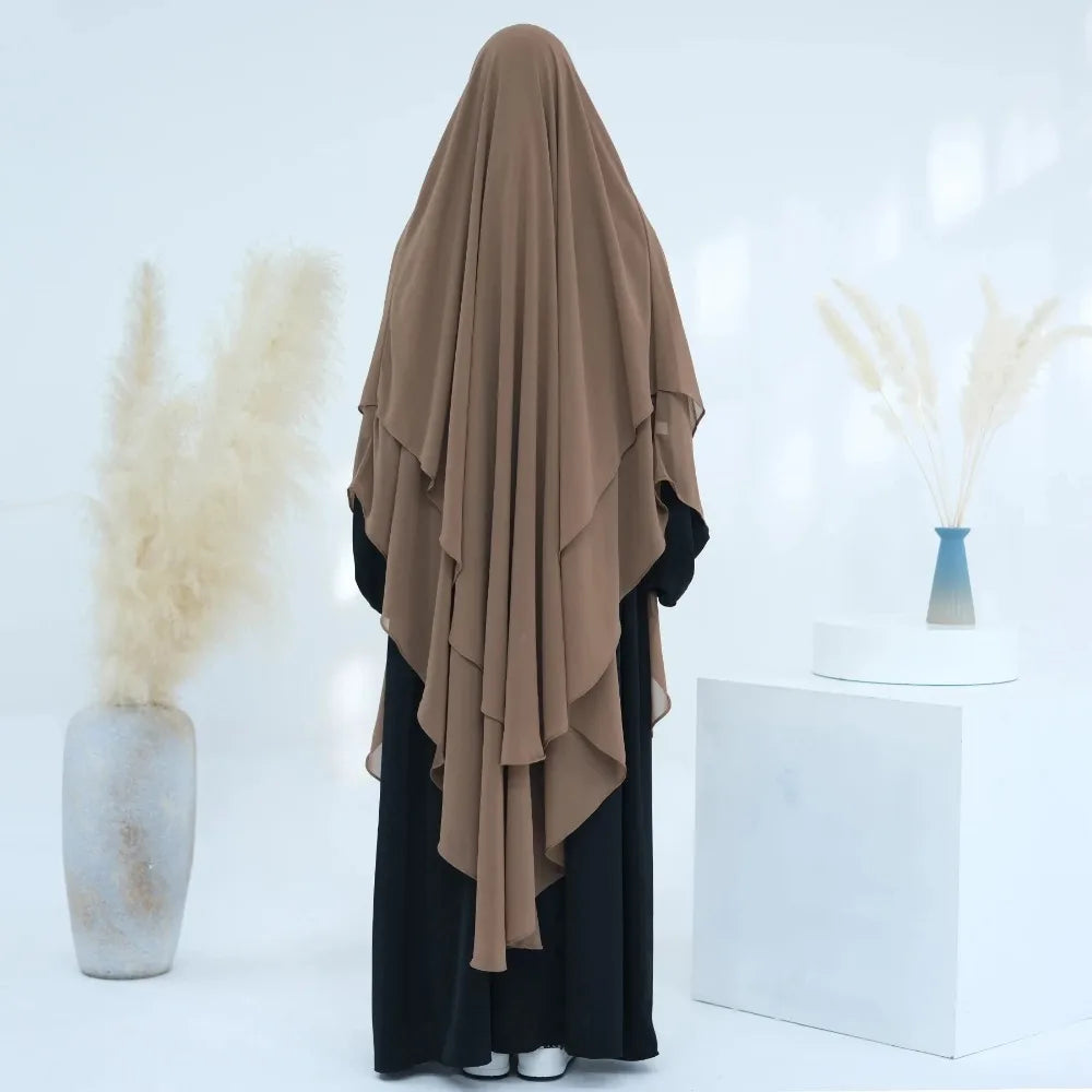 Brauner, zweilagiger Chiffon-Niqab-Kopftuch vor weißem Hintergrund mit getrockneten Blumenarrangements.