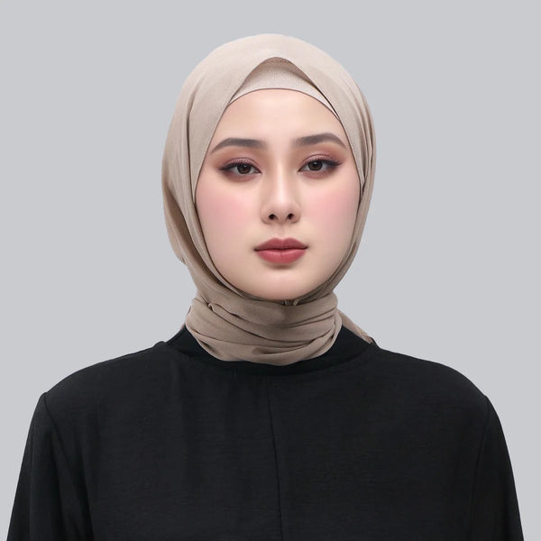 A woman wearing a beige chiffon hijab shawl with a magnetic buckle and a black top.