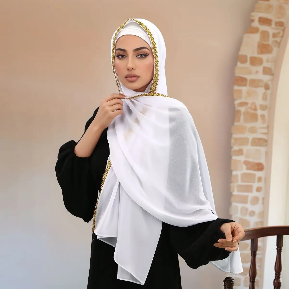 Una mujer vistiendo un elegante hijab de gasa blanca con detalles de pedrería dorada y un atuendo negro.