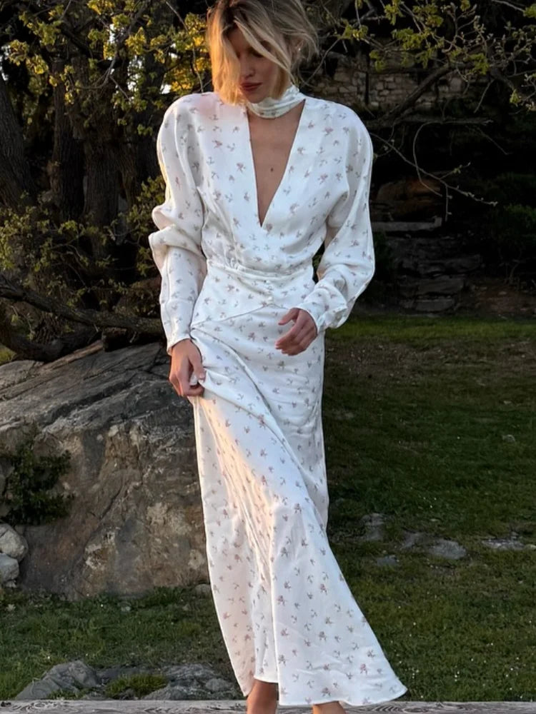 Una mujer vistiendo un vestido largo de satén con estampado floral blanco y escote en V y mangas abullonadas al aire libre.