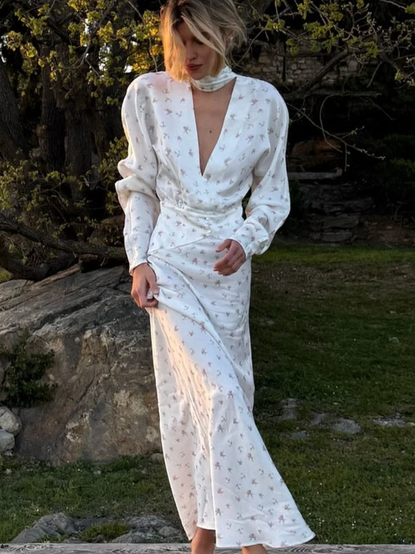 A woman wearing a white satin floral print maxi dress with a deep V-neck and puffed sleeves outdoors.
