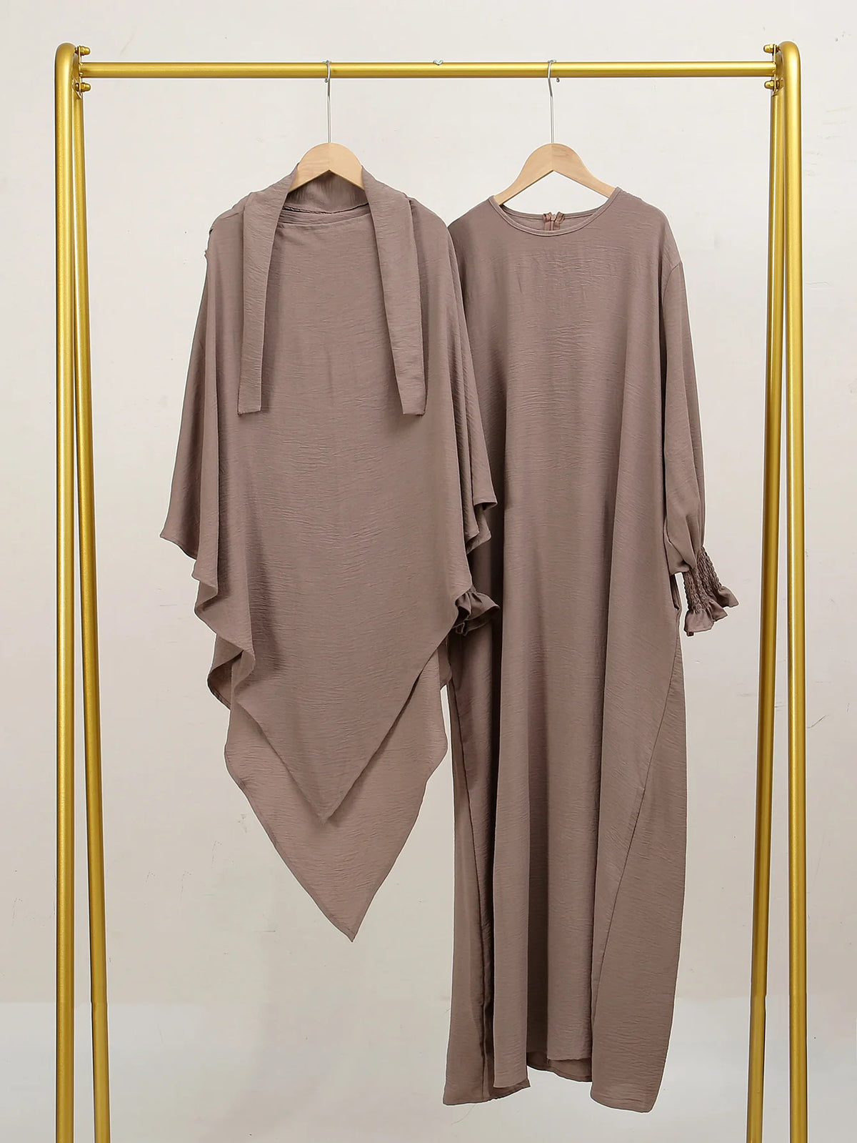 A beige elegant two-piece abaya and khimar set displayed on a gold hanger against a light background.