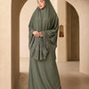 Eine Frau in einem eleganten, mehrlagigen Spitzen-Khimar-Abaya-Set in olivgrün steht in einem hellen Gewölbe-Flur.