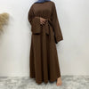 Eine Frau trägt eine elegante, lange braune Maxi-Abaya mit Ärmeln und einem Gürteldetail.