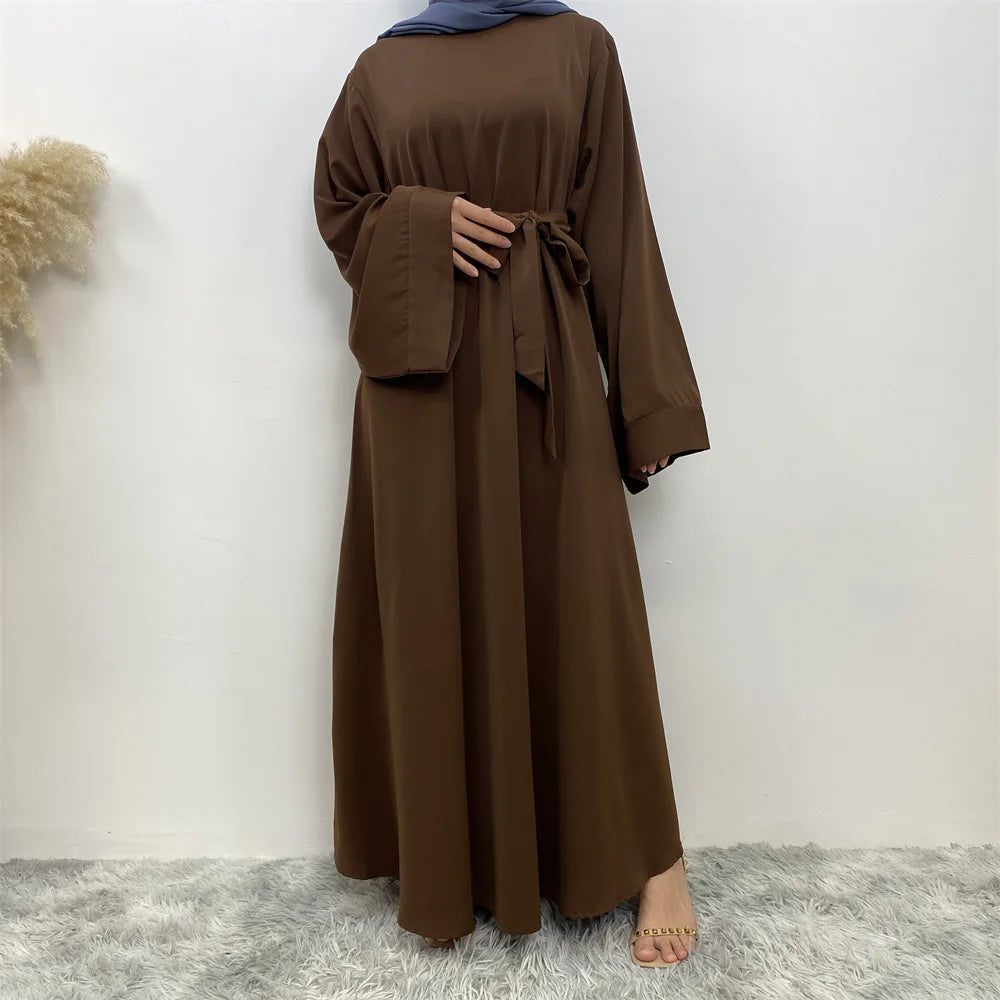 Eine Frau trägt eine elegante, lange braune Maxi-Abaya mit Ärmeln und einem Gürteldetail.
