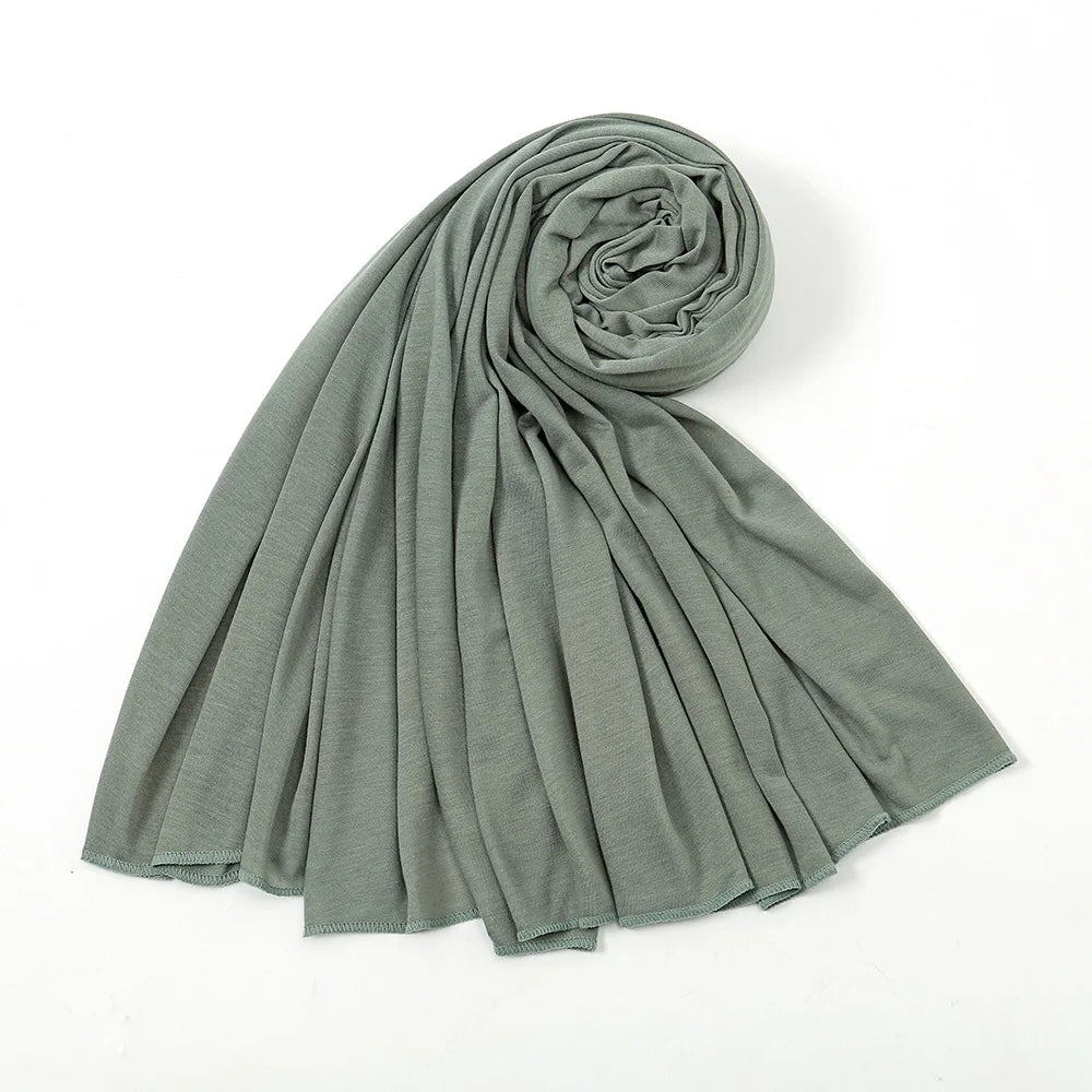 Un foulard hijab en jersey de coton vert sauge, roulé et drapé, montrant sa texture.