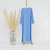 Vestido abaya azul claro y holgado colgado en una percha junto a un jarrón de pampas grass beige seco.