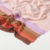 Ein Stapel hochwertiger Chiffon-Hijabs in verschiedenen Pastell- und Erdtönen, darunter Rosa, Mauve, Terrakotta und Beige.