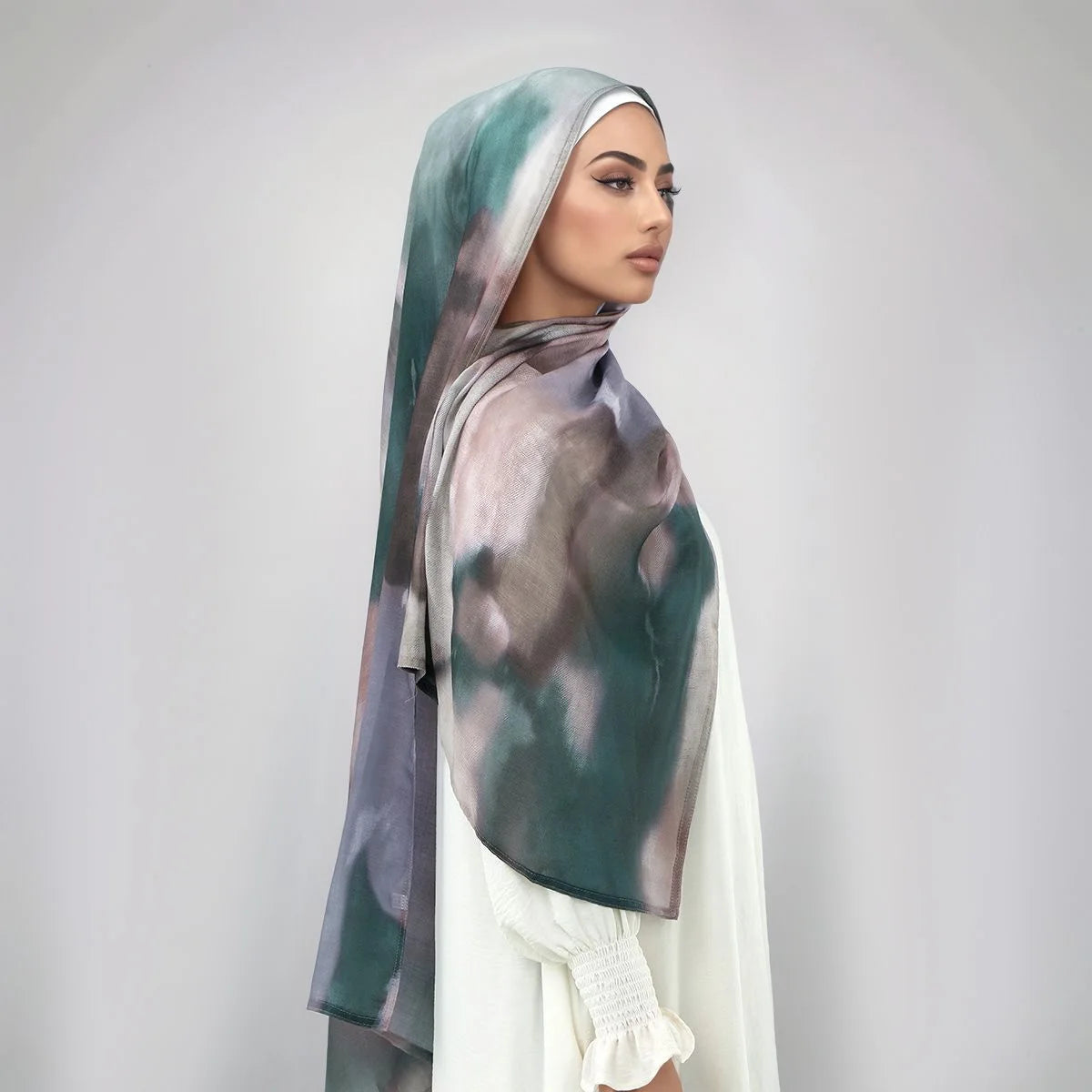 Eine Frau trägt einen Wasserfarbendruck-Baumwoll-Leinen-Hijab-Schal in Grau- und Grüntönen.