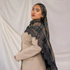 A woman wearing a beige blazer and a plaid hijab scarf with black lace detailing against a white background.