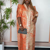 A woman wearing an orange satin kaftan abaya with gold embroidery and matching jewelry.