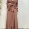 Eine Frau trägt ein fließendes, offenes Abaya-Kaftan in staubrosa mit einem weißen Hijab.