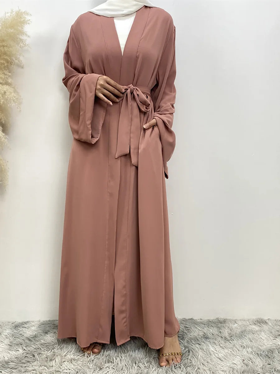 Eine Frau trägt ein fließendes, offenes Abaya-Kaftan in staubrosa mit einem weißen Hijab.