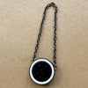 Collar de cadena plateada con un colgante de cuero acolchado redondo negro sobre fondo marrón.