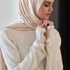 Una mujer vistiendo un pañuelo de hijab de jersey premium beige y una blusa blanca de manga larga.