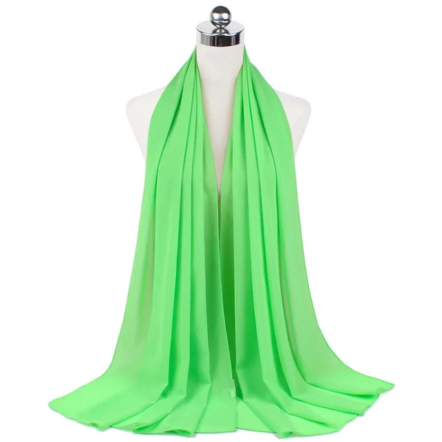 A bright lime green chiffon hijab scarf draped around a mannequin's neck.