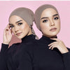 Una mujer vistiendo un elegante turbante de hijab modal beige y una blusa de cuello alto negra.