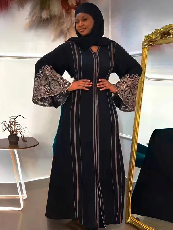 A woman wearing a black abaya dress with long sleeves and embroidered cuffs, standing in front of a gold-framed mirror.