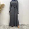 Una elegante abaya de encaje gris carbón completa para mujeres, mostrada de pie contra una pared blanca.
