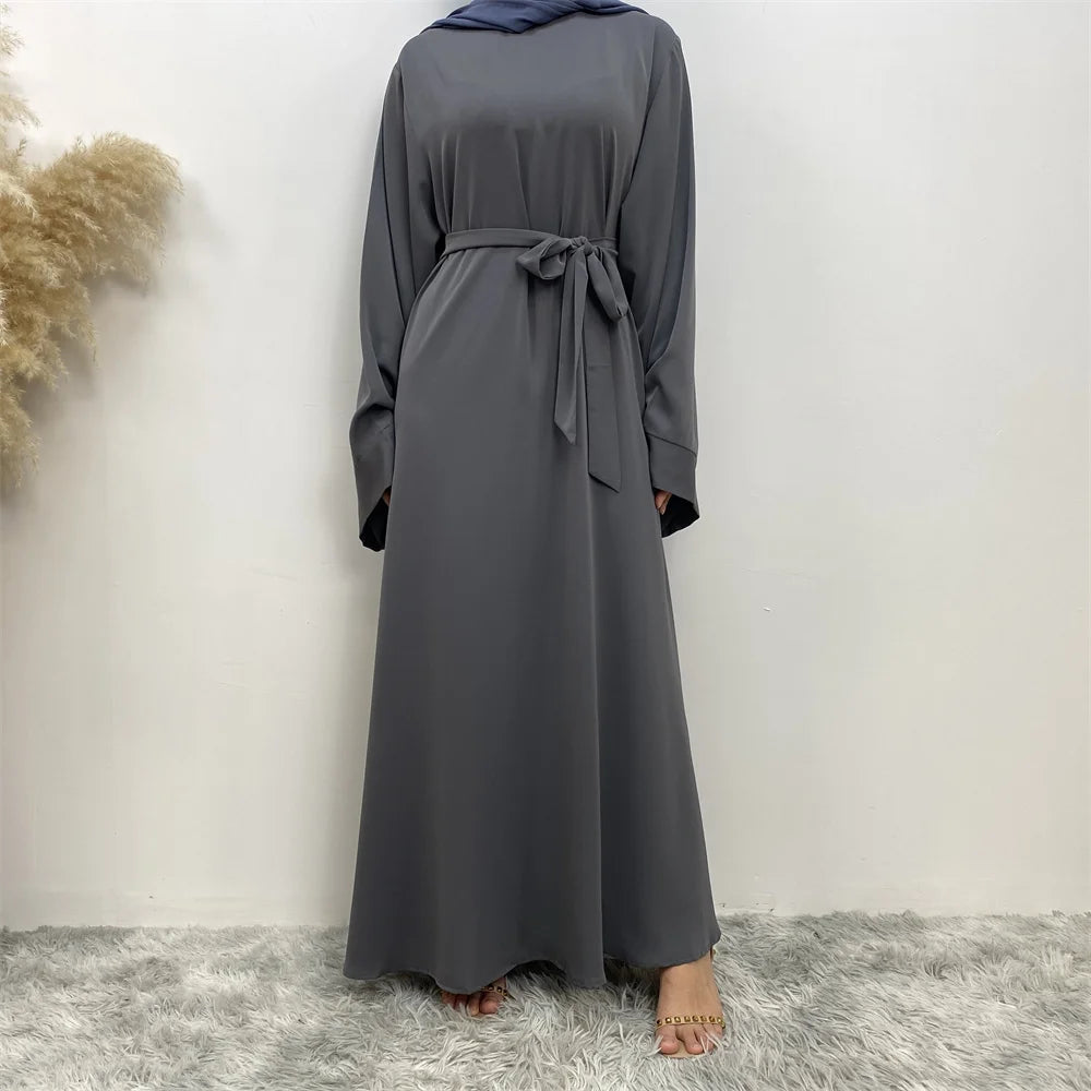 Una elegante abaya de encaje gris carbón completa para mujeres, mostrada de pie contra una pared blanca.
