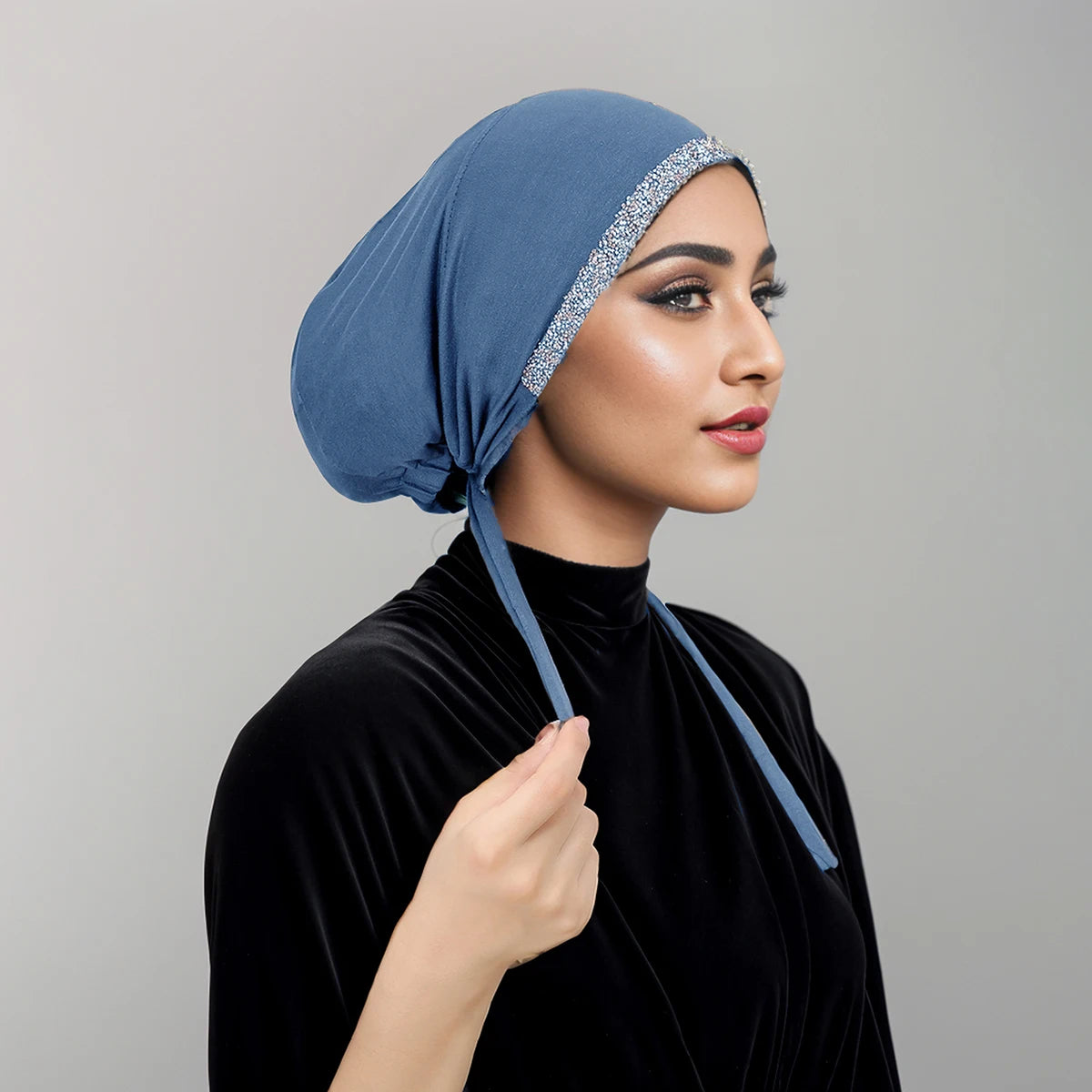 Eine Frau trägt eine blaue Samt-Hijab-Kappe mit silbernen Pailletten und ein schwarzes Samt-Oberteil.