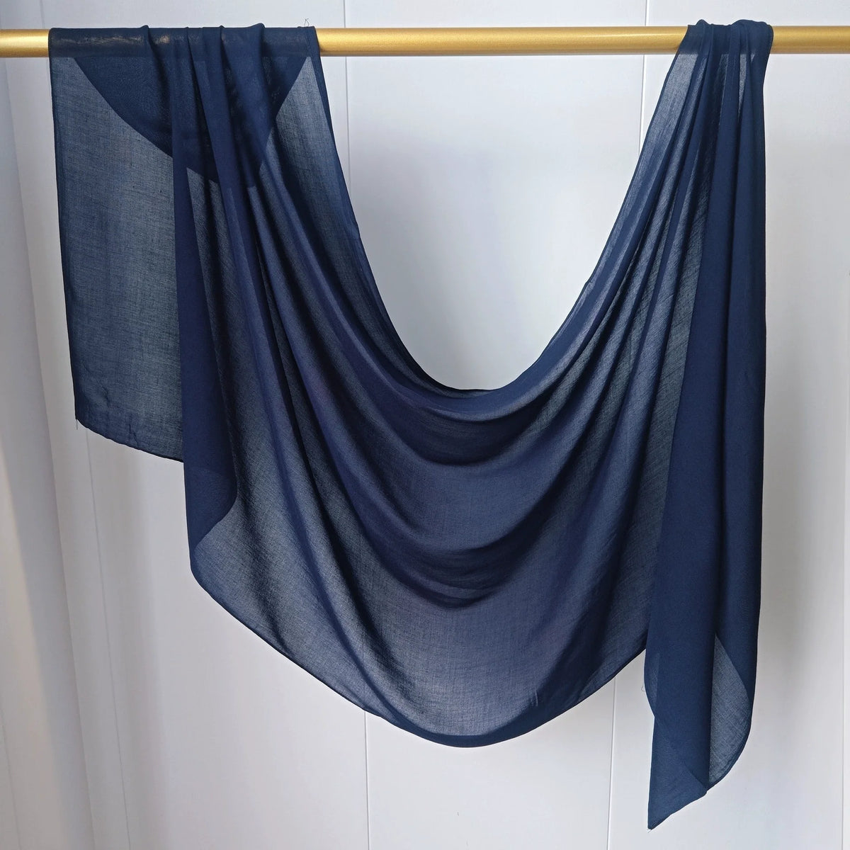 Foulard hijab en mousseline bleu foncé drapé sur un cintre en bois.
