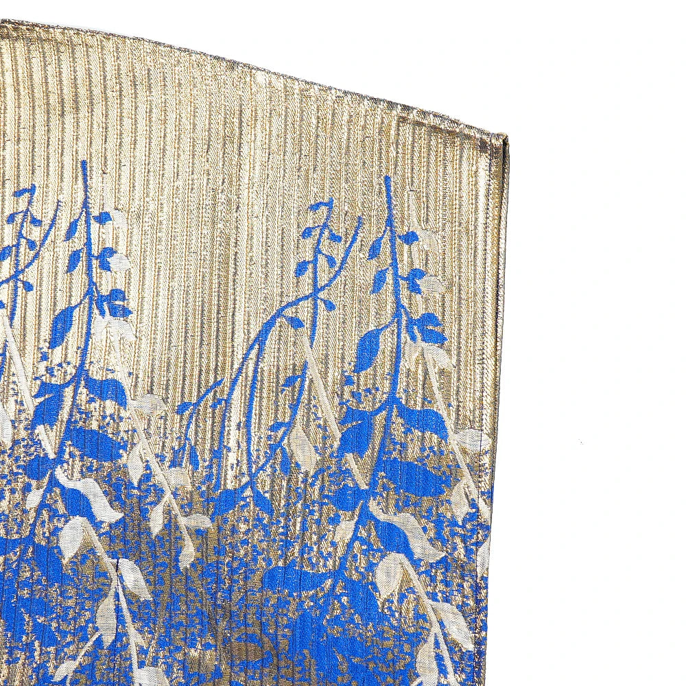 Nahaufnahme eines traditionellen afrikanischen Dashiki Maxi-Kleidstoffs mit blau-goldenen Blattmustern auf beigem Stoff.
