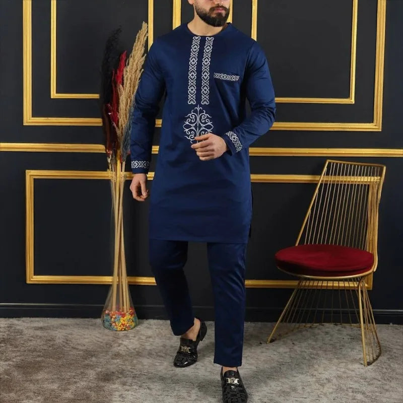 Un homme portant un costume de mariage musulman traditionnel africain bleu marine avec broderies et pantalons sombres.