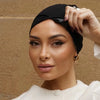 Une femme portant un foulard turban élastique noir, regardant directement l'appareil photo.